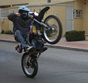 Un tipo haciendo un caballito por la calle con la moto.